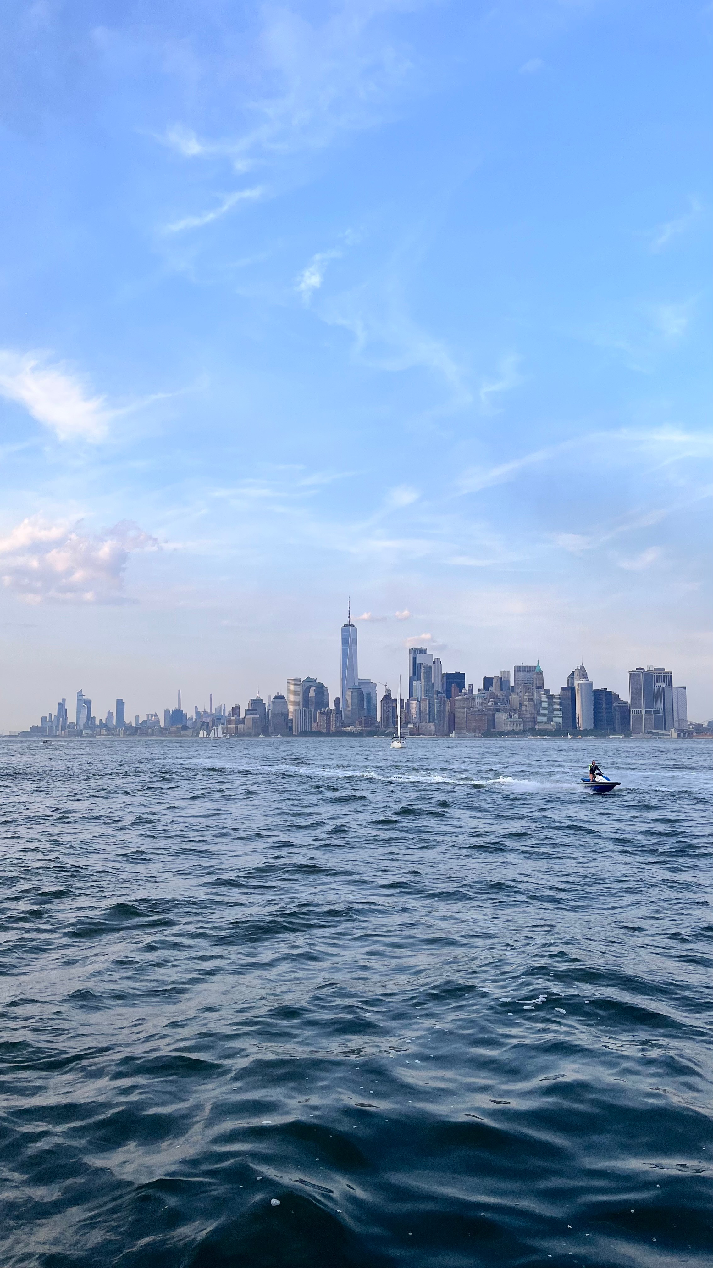 In the foreground, the sea with jet skis, while New York City is in the background.