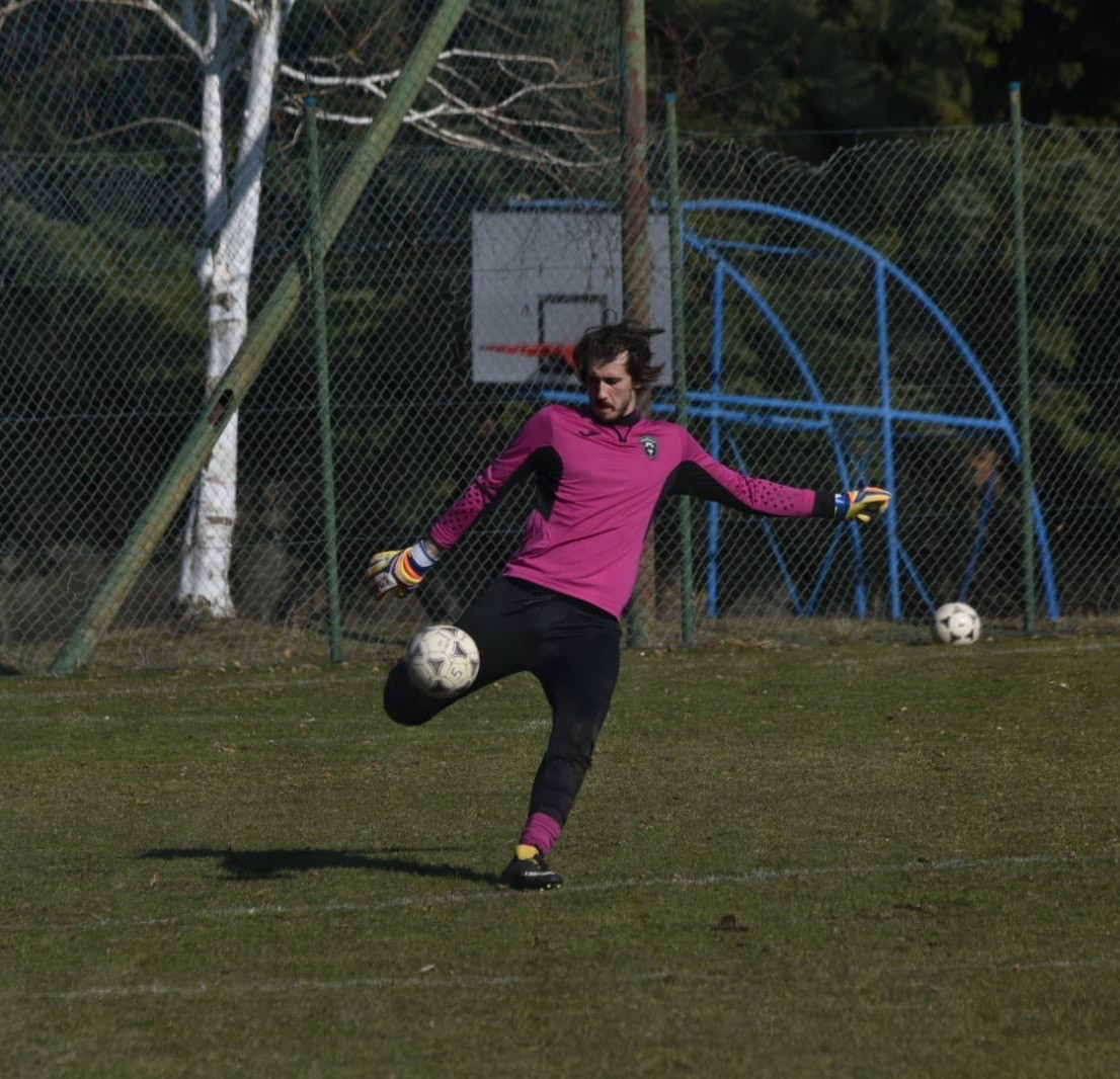 A boy dressed as a soccer goalkeeper kicking a ball.