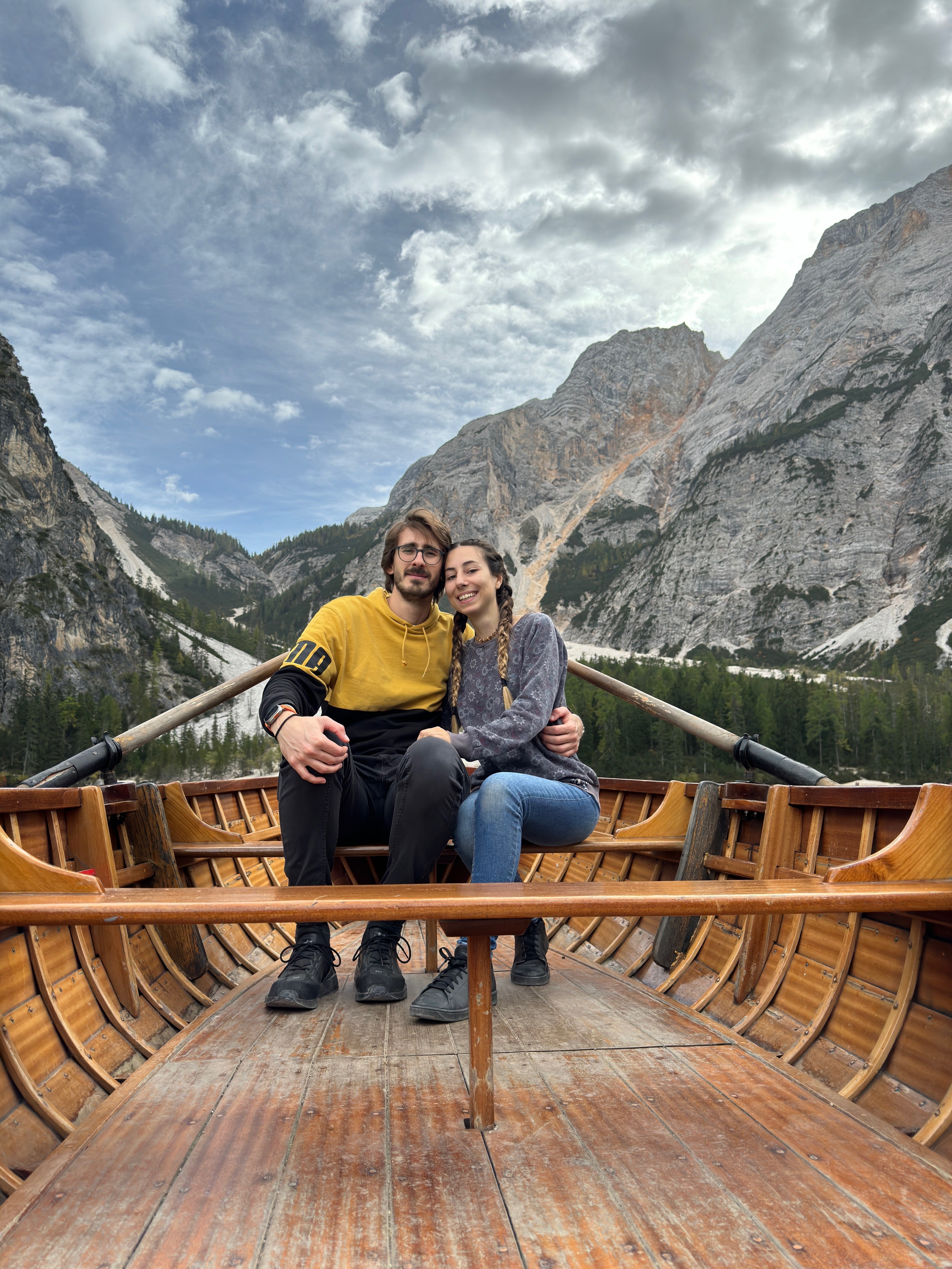 A boy and a girl hugging on a rowboat. The mountains are in the background.