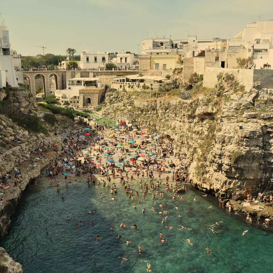 A very crowded rocky beach. In the background, there are some brick structures.
